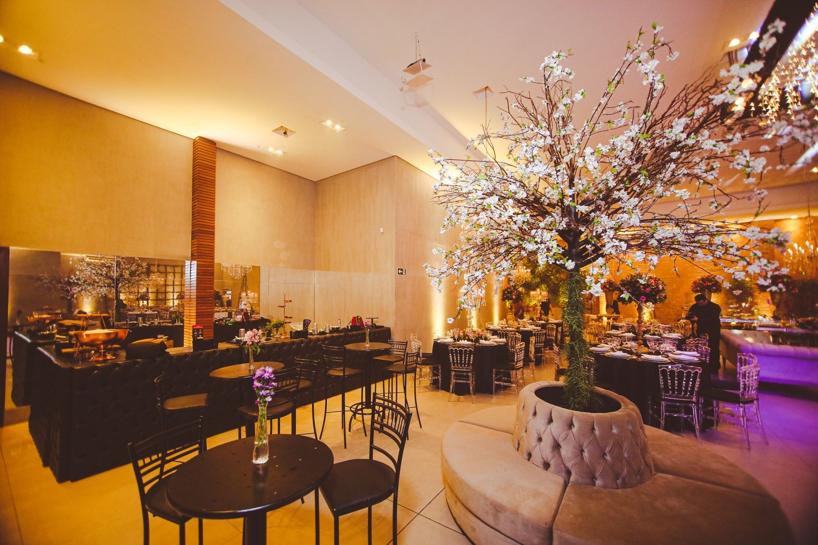 The hall's tufted bar counter and cocktail tables, with a blossom tree set into a circular upholstered bench